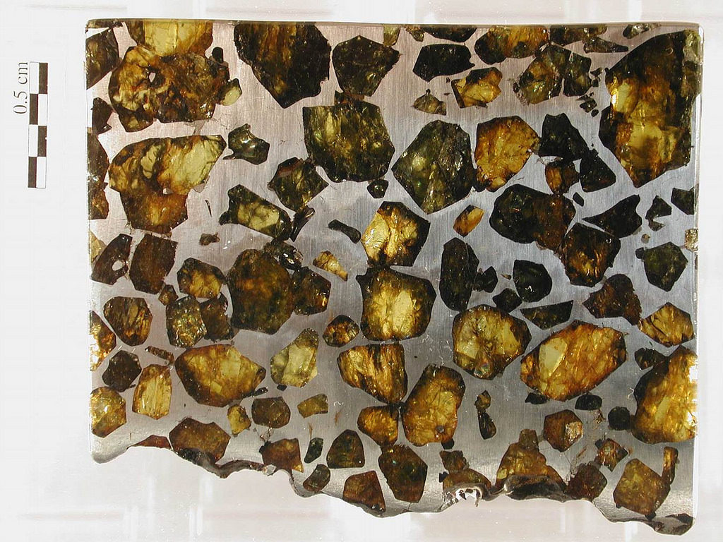 Cut and polished slab of a stony-iron meteorite called a pallasite, thought to have formed in a collision that smashed mantle rocks against the metal core of an asteroid early in the solar system's history. Green and brown crystals are the mineral olivine. The metal between the olivine crystals is an iron-nickel mineral. _Source: Muséum de Toulouse (2012) CC BY-NC 2.0 [view source](https://flic.kr/p/czLSPb)_