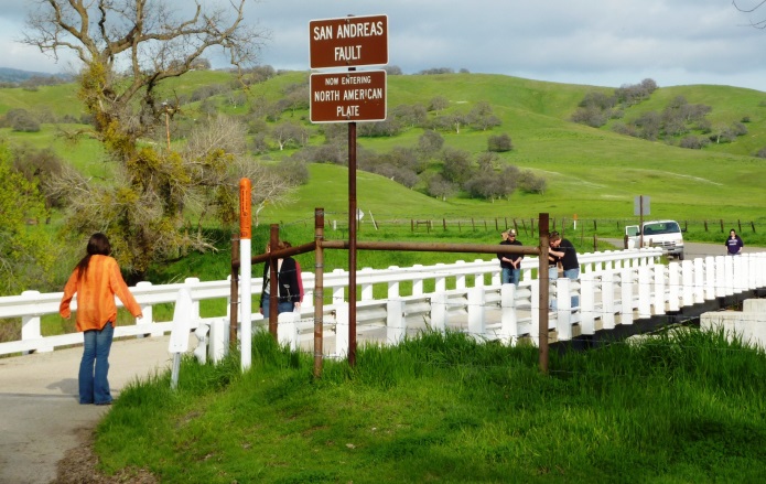 The San Andreas Fault at Parkfield in central California. The person with the orange shirt is standing on the Pacific Plate and the person at the far side of the bridge is on the North American Plate. The bridge is designed to slide on its foundation. _Source: Steven Earle (2015) CC BY 4.0 _[_view source_](http://opentextbc.ca/geology/wp-content/uploads/sites/110/2015/07/image063.jpg)