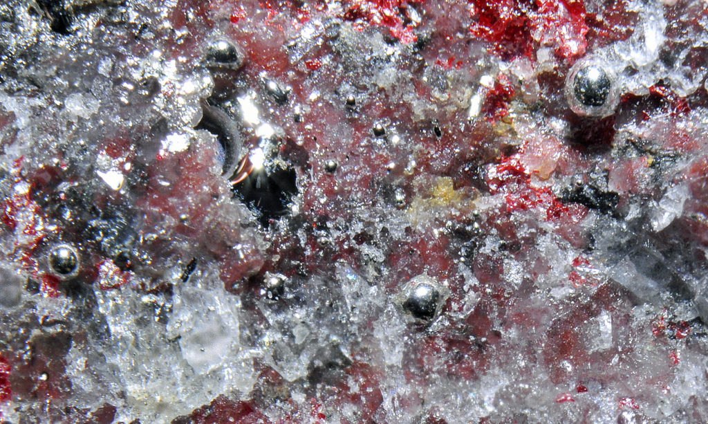 Droplets of native mercury (pure mercury, Hg), also called quicksilver, amid waxy red crystals of cinnabar (HgS). Cinnabar is a mercury ore mineral. _Source: Parent Géry (2012) CC BY-SA 3.0 [view source](https://commons.wikimedia.org/wiki/File:Mercure,_cinabre_3.jpeg)_