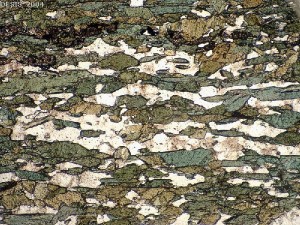Amphibolite in thin section (2mm field of view), derived from metamorphism of a mafic igneous rock. Green crystals are the amphibole hornblende, and colourless crystals are plagioclase feldspar. Note horizontal crystal alignment. _Source: D.J. Waters, University of Oxford [view source](https://www.earth.ox.ac.uk/~oesis/micro/medium/amphibolite_pm20-28.jpg)/ [view context](https://www.earth.ox.ac.uk/~oesis/micro/index.html). Click the image for original figure caption and terms of use._