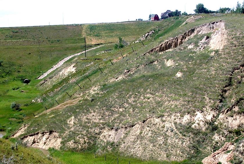 A slump along the banks of a small coulee near Lethbridge, Alberta. The main head-scarp is clearly visible at the top, and a second smaller one is visible about a quarter of the way down the slope. The toe of the slump is being eroded by the seasonal stream that created the coulee. _Source: Steven Earle (2015) CC BY 4.0. [View source](https://opentextbc.ca/geology/) _