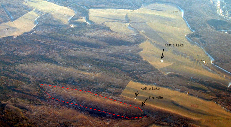 Drumlins and kettle lakes viewed from the air near Fort St John, BC. There are numerous drumlins in the image; one is outlined in red. Can you spot the others? Note the alignment of the long axes of the drumlins. _Source: Joyce McBeth (2002) CC-BY 4.0._ __Click the image for a higher resolution version__.